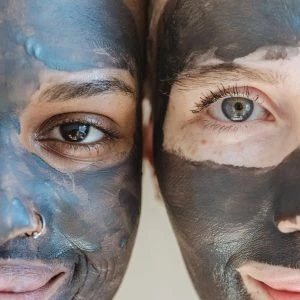 Two women with face masks, one with dark skin and one with light skin, smiling close-up.