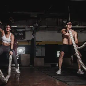 People performing battle rope exercises in a gym setting.