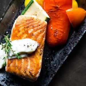 Delicious grilled salmon served with roasted vegetables and a herb garnish on a black rectangular pl.
