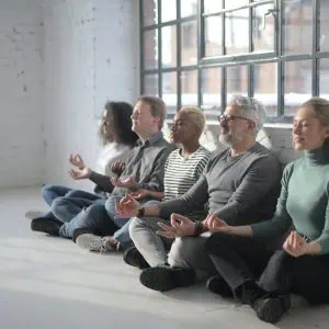 Diverse group meditating in a bright, spacious room for mindfulness and well-being.