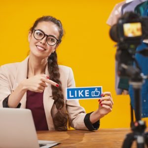 Portrait of contemporary young woman holding LIKE word and smiling at camera while filming video for beauty and lifestyle channel, copy space