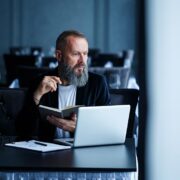 Businessman with a beard working on a laptop in a modern cafe, possibly during a remote work or onli.