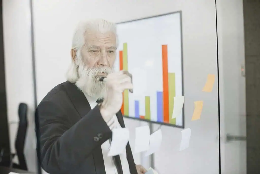 Elderly man pointing at bar chart on screen in office.
