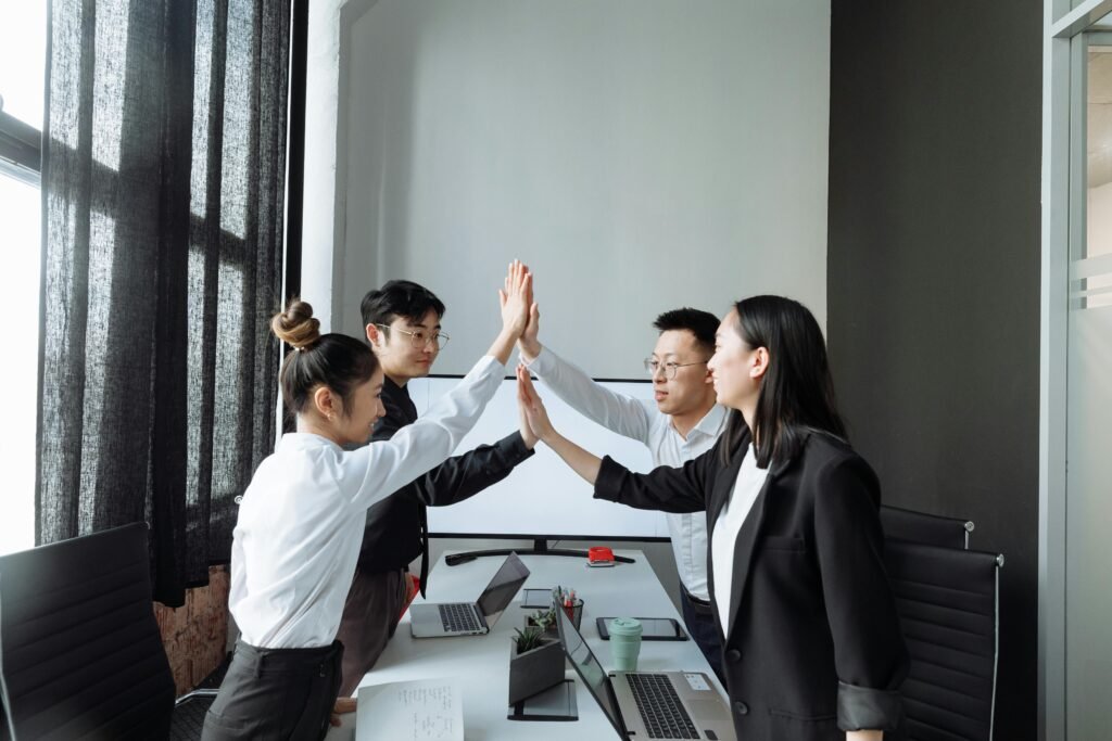 Four multicultural colleagues in a modern office high-fiving, celebrating teamwork and success.