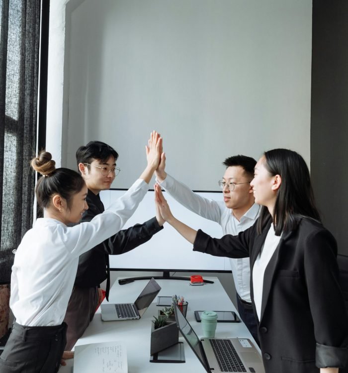 Four colleagues in a modern office high-fiving, celebrating teamwork and success.