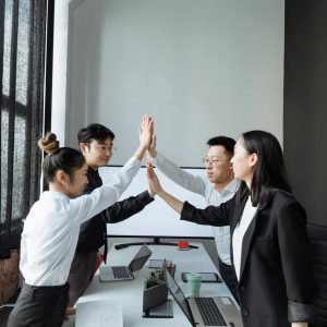 Diverse business team celebrating success with high-five in contemporary office setting.