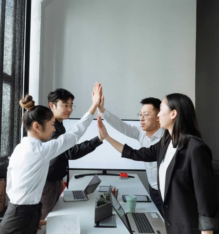 Diverse business team celebrating success with high-five in contemporary office setting.